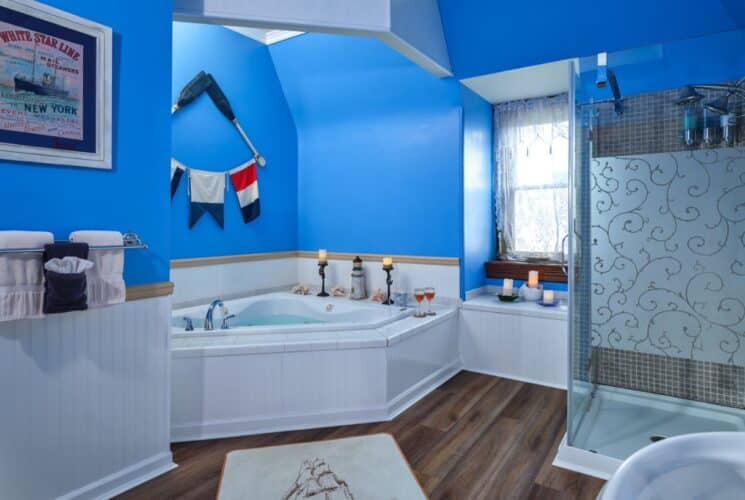 Bathroom with bright blue walls, hardwood flooring, standup shower, small window nook, and white two-person jacuzzi whirlpool tub