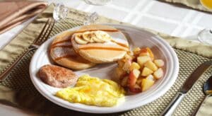 White plate with scrambled eggs, sausage, home-made cinnamon chip pancakes, and seasoned potatoes for breakfast at Spencer House Bed & Breakfast, Erie, PA