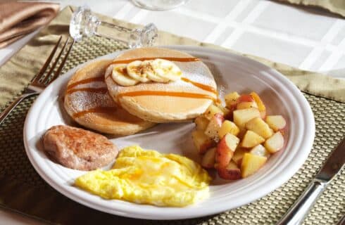 White plate with scrambled eggs, sausage, pancakes, and fried potatoes