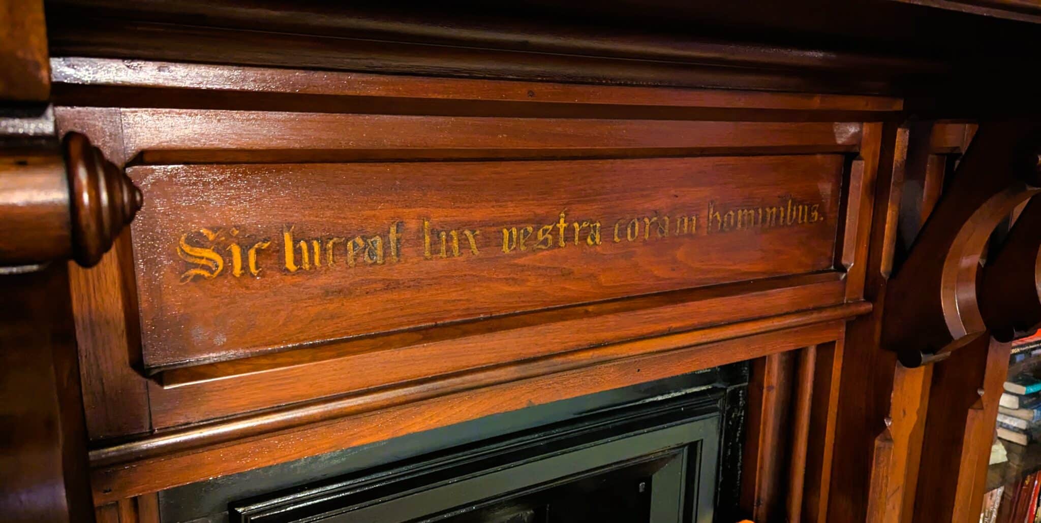 Close-up of the Latin motto carved and gilded into the library fireplace mantel at Spencer House, reading ‘Sic luceat lux vestra coram hominibus,’ Matthew 5:16, the inspiration for Shining Light Hospitality’s name
