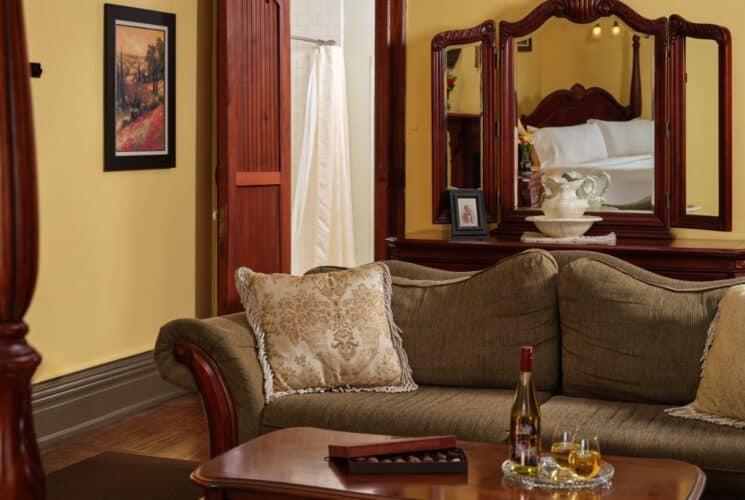 Large bedroom suite with yellow walls, tan sofa, coffee table with a bottle of wine and a box of chocolates and a dark wood dresser