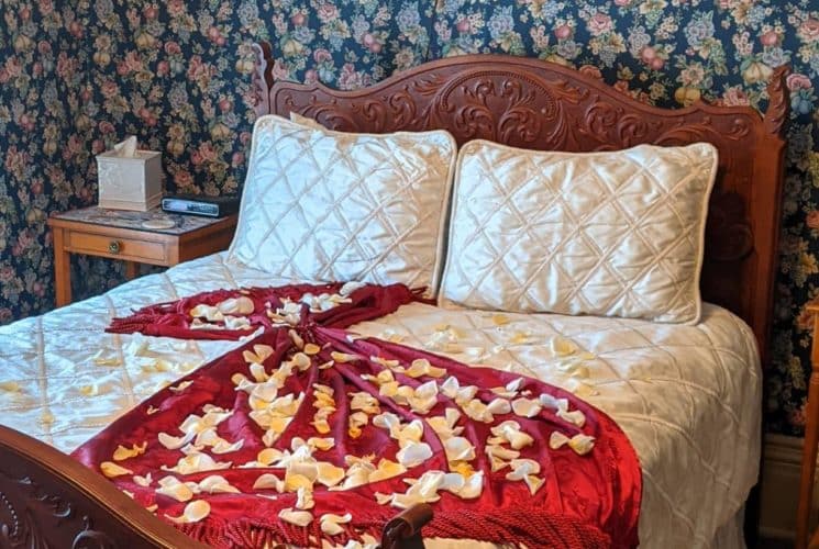 Bedroom with wooden bed, white bedding, and a red blanket with sprinkled white petals on it