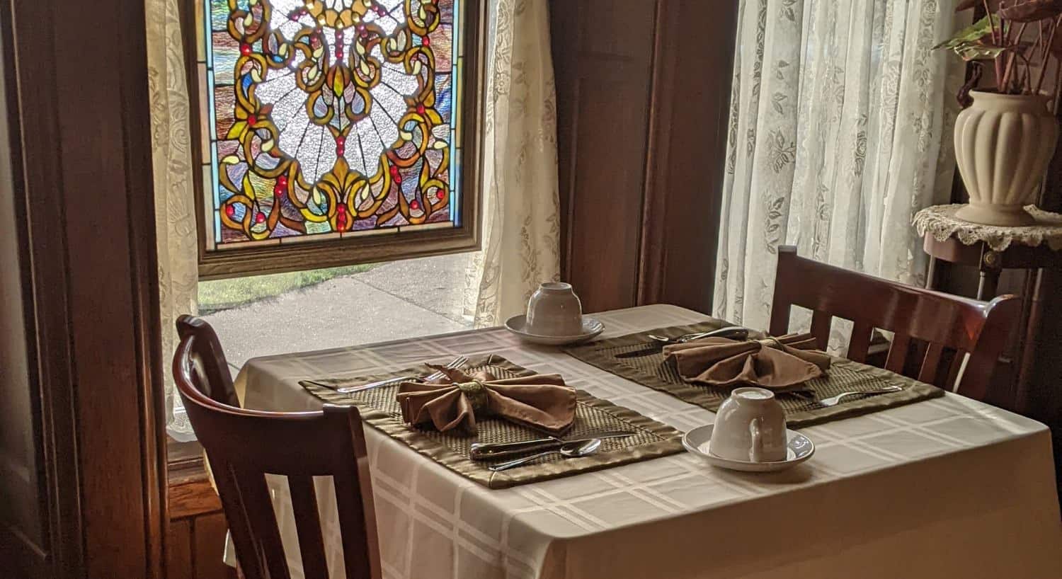 Table with two place settings next to window with a hanging framed stained glass piece of art