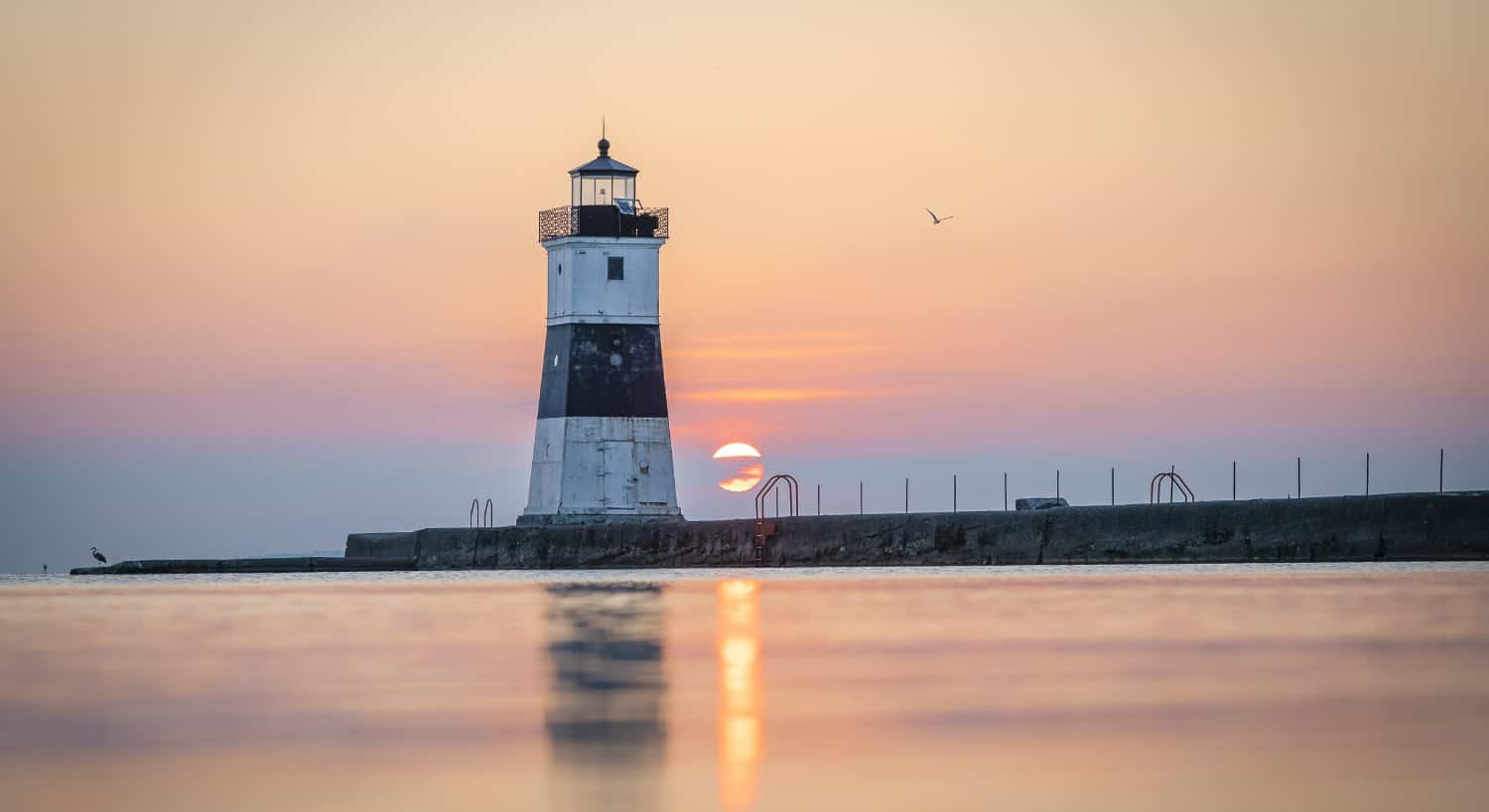 Lighthouse surrounded by calm water with a setting sun covered by clouds in the background