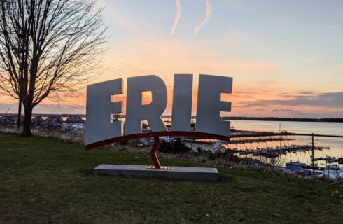 Large Erie sign sitting in green grass on a hill overlooking a harbor