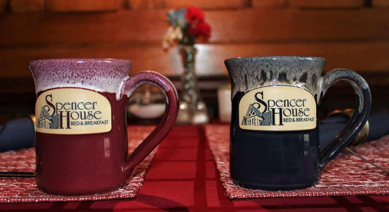 Close up view of red and navy stoneware cups with the Spencer House Bed & Breakfast logo