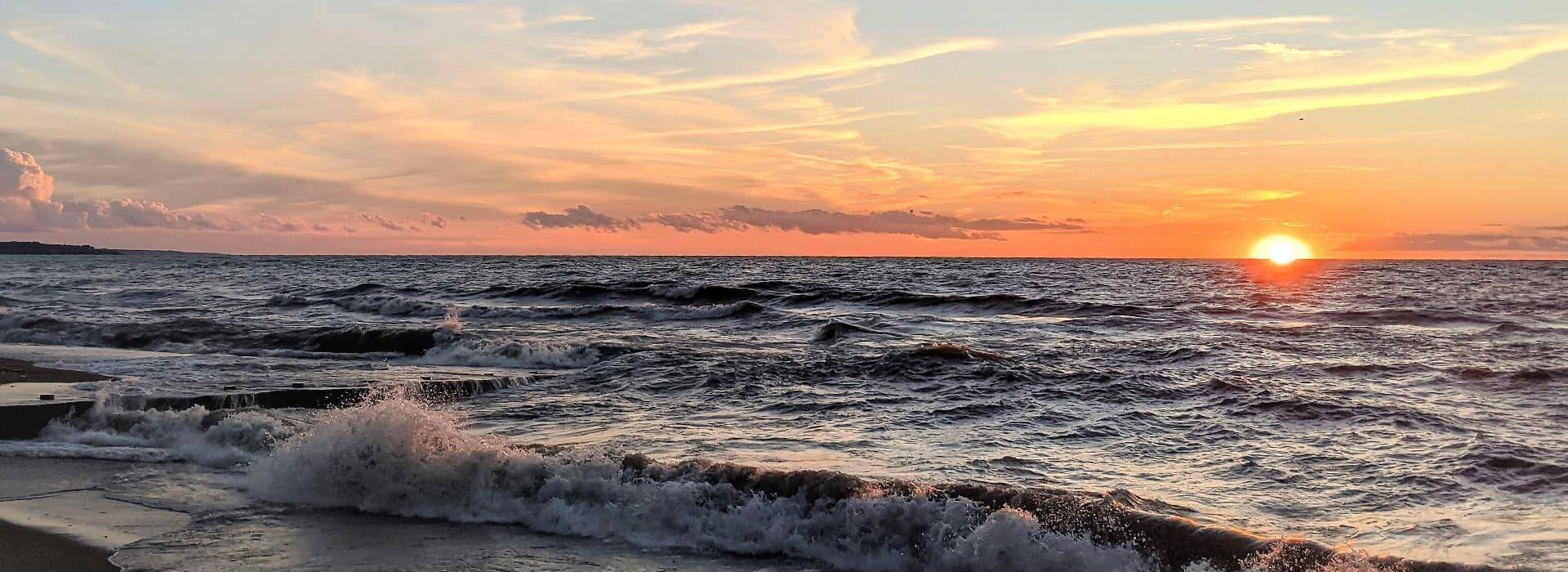 Rolling waves hitting a beach with the sun setting in the background