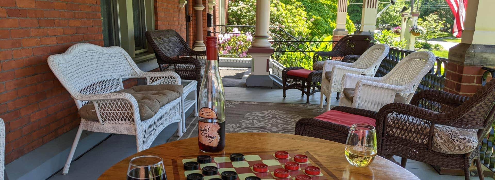 Front porch with white and brown wicker patio furniture and wooden table set up with checkers, a bottle of wine, and glasses with red and white wine